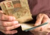 Primeira parcela do 13º salário será paga nesta semana — Veja prazos e regras Mão segurando cédulas