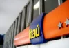 Itaú aprova pagamento de R$ 23,4 bilhões em proventos: Veja quem recebe e quando Fachada de agência do Itaú com logotipo iluminado durante anúncio de pagamento de proventos.