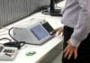 TSE inicia testes de vulnerabilidade das urnas para as eleições de 2026 Técnicos examinando urna eletrônica em laboratório durante testes de segurança.